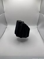 Side view showing the vertical striations and rough texture of the black tourmaline specimen on a white background.