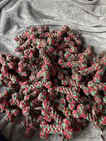 Pile of 70 braided red and green cotton bone-shaped pet toys with brown patterned ribbons on cozy fabric background.