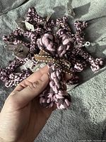 Close-up photo showing individual bone-shaped cotton toys being held in hand, with visible texture and colors of the braided cotton and decorative ribbon.