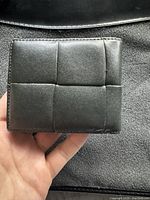 Front exterior of wallet showing signature padded cassette weave black leather design held in hand.