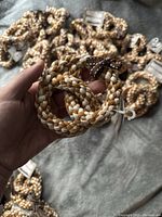 Close-up of a hand holding one pretzel-shaped rope toy in beige and white cotton with a brown polka dot ribbon, several other toys in the background.