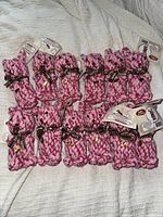 Twelve pink woven rope bunny shaped dog toys laid out on a light fabric surface, each with brown ribbon tied around the neck and attached label.