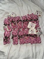 Set of 12 pink rope bunny-shaped dog toys with brown ribbon bows, laid out on a white textured surface.