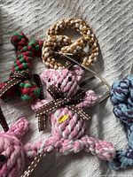 Multiple new rope dog toys in varied colors and shapes including bones, rings, and animal figures laid on a textured fabric surface.