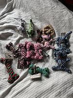 Photo showing multiple brand new rope dog toys in pink, blue, green, purple, and brown with white. Shapes include bunnies, bones, and twisted figures with decorative ribbons.