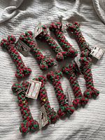 Lot of 10 large, braided dog bone toys arranged on a fabric, each red and green cotton color, tags attached.