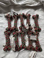 Lot of 10 natural cotton braided red and green dog bone toys arranged together on fabric background.