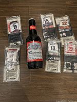 View of the Budweiser tall glass beer bottle surrounded by six McDonald's mini jersey collectibles in original clear plastic packaging, displayed on a brown wooden floor.