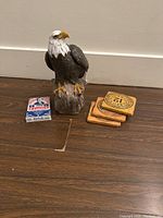 Eagle statue, George Bush playing cards, and wooden coasters shown together on floor.