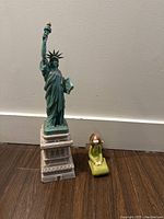 Front view of the Liberty Statue replica with the green angel sitting statue next to it for size comparison.