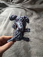 Close-up photo of one animal-shaped pet toy made from twisted natural cotton rope in blue and purple colors held by hand to show scale and material detail.