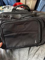 Front view of the black Travel Pro carry on bag showing multiple zippered compartments and the shoulder strap attachment.