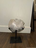 Front view of white quartz crystal cluster on metal stand against wall on floor.