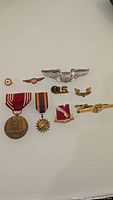 Top down view of various vintage US military medals and pins arranged on white surface showing detailed design of metal and ribbons.