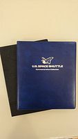 Blue book with silver text reading 'U.S. Space Shuttle Commemorative Collection' on cover, and a black book beneath it.