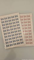 Two sheets of stamps together showing blue 14 cent and red 30 cent denominations sealed in plastic sleeves on a flat surface.