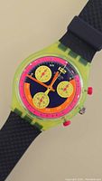 Watch face showing translucent lime green case, navy blue dial, neon pink track, yellow subdials, orange hands and pink pushers