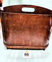 Front view of vintage bentwood magazine holder showing curved wooden panels and cutout handle, with some surface wear and scratches visible.