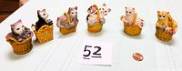 Front view of all six miniature cat figurines in ceramic wicker baskets, showing varying colors and poses.
