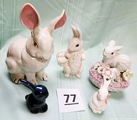 Photo showing all five ceramic bunny figurines arranged on a cloth background with item number 77 card for reference.