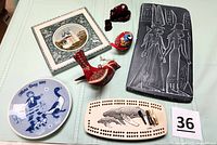 Photo showing the entire assortment of nine souvenir items from seven countries including cribbage game board, Egyptian plaque, Mother's Day plate, Russian tile, Mexican bird ornament, Hungarian egg, and Chinese figurines.