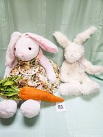 Both bunnies seated on green fabric background with stuffed carrot shown in front