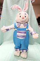 Front view of large cloth boy rabbit figurine in blue overalls and striped shirt with open arms and smiling face.