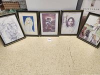 Five framed Lord of the Rings character sketches on the floor, arranged side-by-side showing diverse characters from the series.