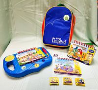 Photo showing My First LeapPad learning tablet, four interactive books, three cartridges, and blue backpack carrying case