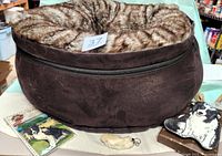 Photo showing plush donut-shaped pet bed with removable pillow inside, brown faux leather exterior and faux fur interior, plus Border Collie light switch plate and spoon rest in front.