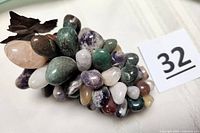 Polished stone grape cluster showing various colors and metal leaf from a side angle.