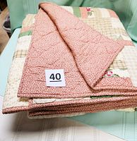 Folded quilt displayed with a visible red floral reverse side and patchwork front with a lot number 40 card on top.
