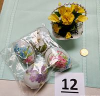 Set of four hollow white decorative eggs with various hand-painted floral designs in a plastic bag next to a penny for size reference.