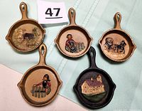 Top view showing the five mini cast iron fry pans, each with a distinct hand-painted image including people, horse and buggy, a covered bridge, and a building.