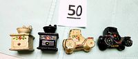 Four miniature cast iron salt and pepper shakers including two Model A cars and two coffee grinders arranged side by side on a light surface with a lot number card '50'. The cars display cream and black color with floral paint details.