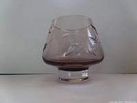 Photo showing front and side view of amethyst-colored bowl or vase with etched leaf and vine pattern, highlighting shape and etching details.