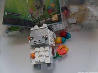 Close-up photo of an assembled white LEGO BrickHeadz sheep with orange, blue, and red accessory pieces attached, showing blocky body and face details.