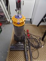 Front view of Dyson Animal vacuum cleaner with yellow cannister and attached hose and power brush head on carpet.