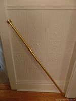 Gold tension rod leaning against a wall, showing full length and circular mounting ends.