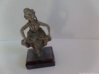 Pewter figurine of woman in a dress standing on a wooden base shown at an angle