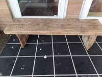 Full view of the rustic barn board bench showing thick plank seat and two solid wooden legs.