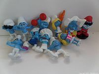 Front view of all 10 Smurf figurines arranged together showing variety of poses and accessories.