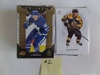 Two hockey cards in penny sleeves displaying Mitch Marner Trilogy card and Brad Marchand SP Authentic card