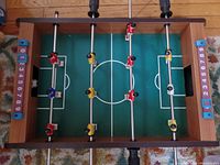 Top view of a wooden tabletop foosball game with green surface, red, yellow, and blue plastic players on rods, and scoreboards on each side