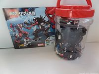 Instruction booklet displayed behind clear plastic tub containing LEGO pieces and partially built Venom mech.