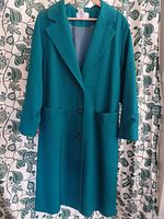 Full front view of vintage turquoise wool coat hanging against floral wallpaper,