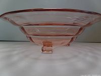 Side view showing pink tinted glass bowl with etched floral and leaf design and one of the three clear glass feet.