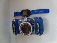 VTech Kidizoom digital camera and kids watch side by side on a white surface, showing the front and strap of the watch.