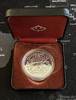 Silver Canadian dollar coin from 1980 in brown velvet-lined display case with a red interior showing a Canadian maple leaf emblem.