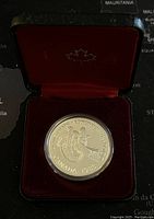Coin in original red velvet lined black case showing front design and maple leaf emblem inside lid